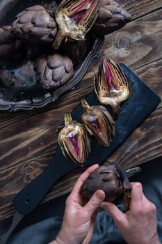 Woman cleaning fresh artichokes and cooking on wooden table, rustic still life top view,concept of healthy eating and fine dining,