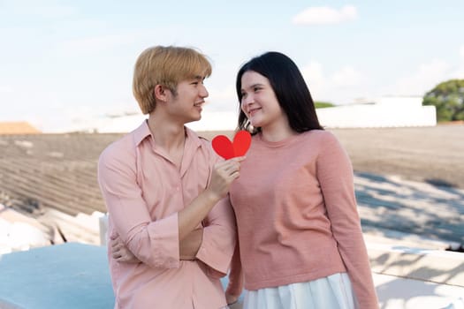 A couple joyfully celebrates their love on Valentine's Day sharing a heart symbol in an urban backdrop.