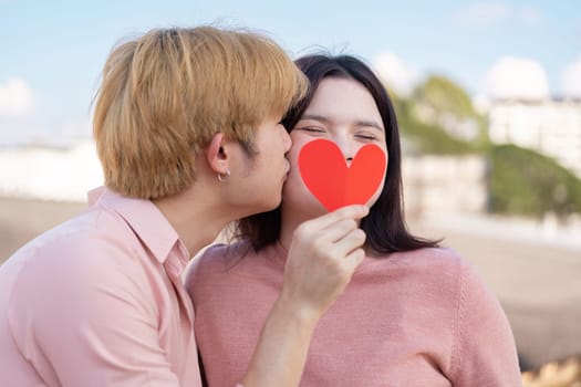 A young couple shares a sweet Valentine moment at the beach showcasing love and joy with a heart cutout.