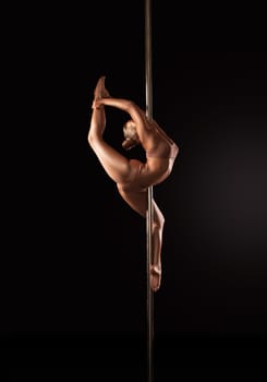 Side view of flexible slim female in underwear dancing sensual dance around pole on black background