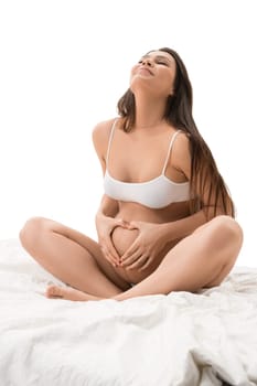 Happy pregnant woman wearing white top sitting on her bed bed isolated shot