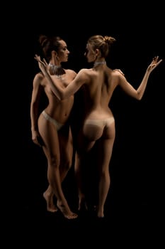 Two gorgeous women topless in fine bijouterie full-length shot against black wall