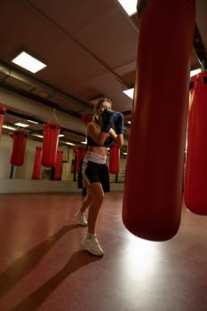 Young blonde in boxing gloves exercising with a punching bag in a gym