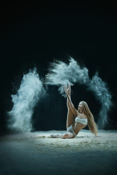 Young blonde sitting in white dust cloud shot in the dark room