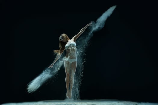 Slim blonde wearing lingerie jumping gracefully in white dust cloud view in the dark room