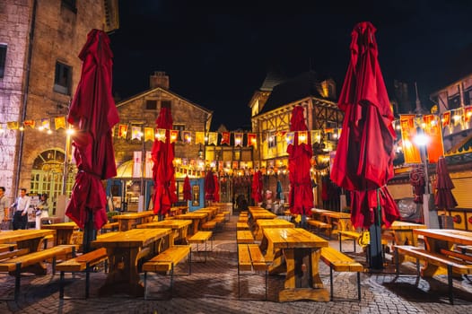 Decorated interior of the festive outdoor cafe street restaurant with wooden tables and benches in night in Ba Na Hills Park. Da Nang, Vietnam - September 13, 2024