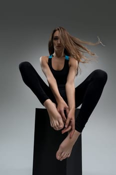 Well-shaped blonde in black sportswear sitting on the cube in the dark room view