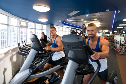 Young sporty males and woman exercising on simulators in a gym