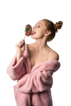 Beautiful nude charming woman with closed eyes in bathrobe licking sweet candy on white background