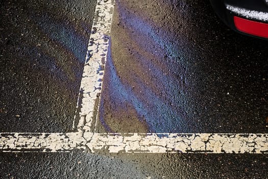 Fuel or oil stain on wet parking lot asphalt, indicated by a white line.