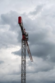 Tower crane with red trim against cloudy sky before thunderstorm captured in realistic photo, urban construction and infrastructure development concept, copy space,