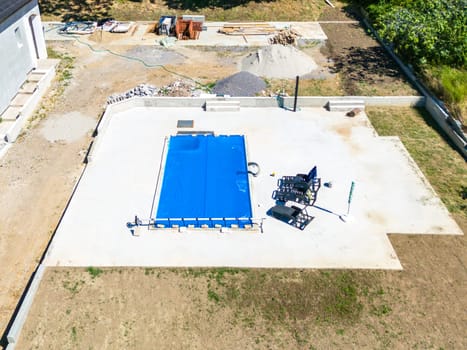 Overview of swimming pool construction with blue pool cover and surrounding groundwork