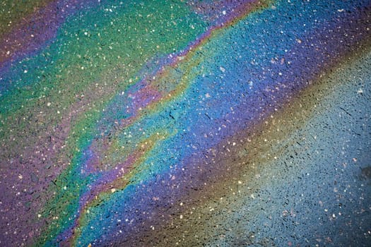 Rainbow-hued oil spill on a paved road, serving as an abstract composition