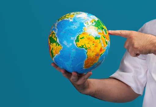 An individual holds a globe and points at a specific location, emphasizing the significance of geography and global exploration. The bright colors of the globe make it visually engaging.