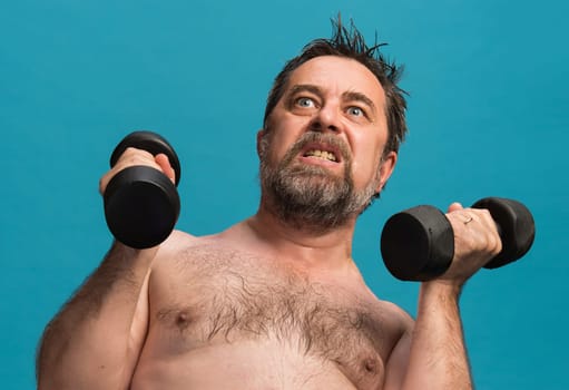 An elderly man exercises with dumbbells, focusing hard as he lifts weights. The bright blue backdrop contrasts with his determined expression and showcases his strength and dedication to fitness.