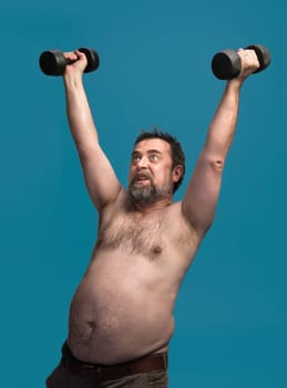 An elderly man with a beard exercises by lifting dumbbells overhead. He appears focused and strong, demonstrating commitment to fitness in a vibrant indoor space.