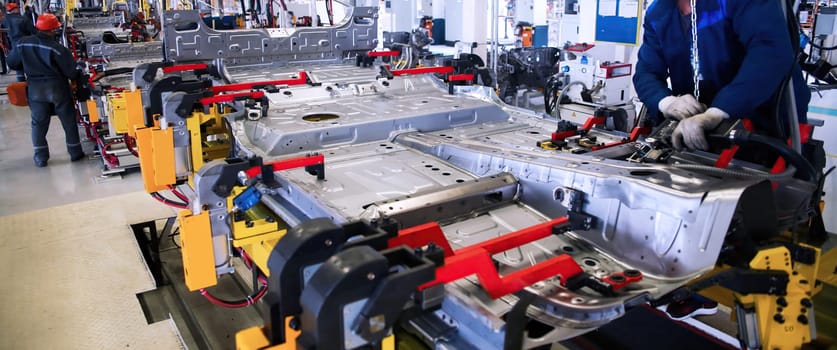 In a bustling manufacturing facility, workers meticulously assemble a vehicle chassis using advanced tools and techniques