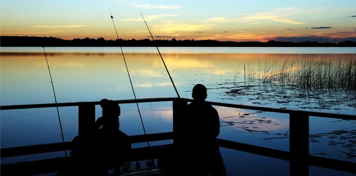 As the sun sets, two fishermen enjoy a peaceful evening on the lake, casting their lines into the water and reflecting on the colorful skies.