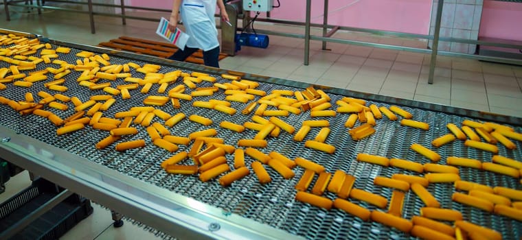 A busy confectionery factory features a cookie production line where golden cookies are continuously transported on a conveyor belt, indicating high output.