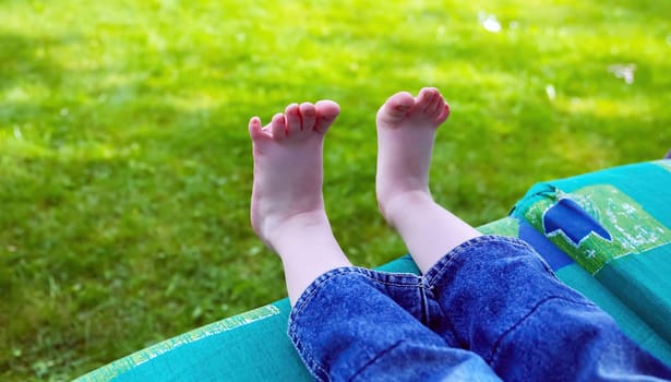 A child is relaxing with bare feet on a soft, green lawn, enjoying the warmth of a sunny afternoon.