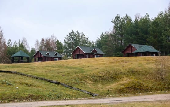 A group of rustic cabins sits on a gentle hillside, surrounded by trees, creating a tranquil atmosphere for relaxation in nature.