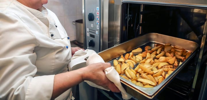 A chef removes a tray of perfectly roasted potatoes from a commercial oven, showcasing culinary skills and kitchen expertise.