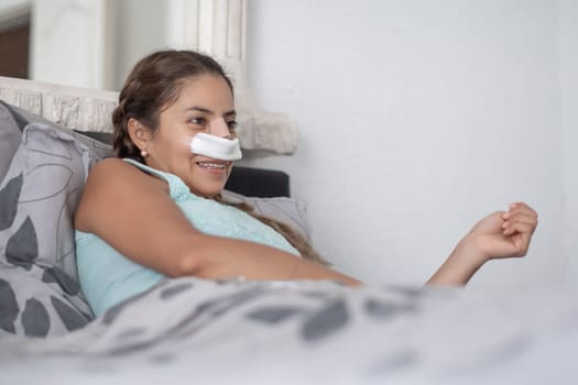 woman lies in bed in casual clothes and with bandages on her face after plastic surgery on her nose, worried and anxious about the result,