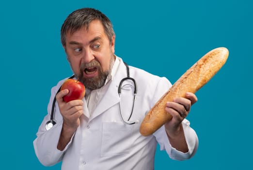 A man in a white lab coat and stethoscope holds a red apple in one hand while looking excitedly at a long baguette in the other.