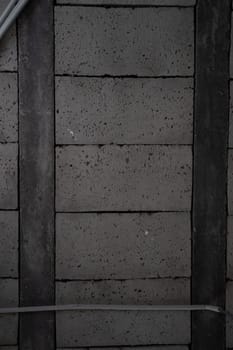 A detailed view of a dark gray cement block wall featuring rough, textured surfaces with horizontal and vertical alignment. An industrial conduit is positioned along the bottom edge of the wall.