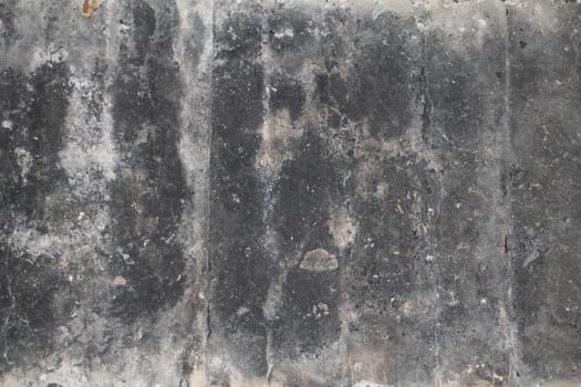 A close-up view of a worn black cement surface featuring uneven textures, stains, and marks. The surface appears aged with patterns of discoloration.