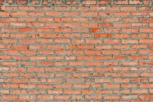 A traditional red brick wall featuring visible imperfections and rugged cement gaps, creating a rustic and raw aesthetic.