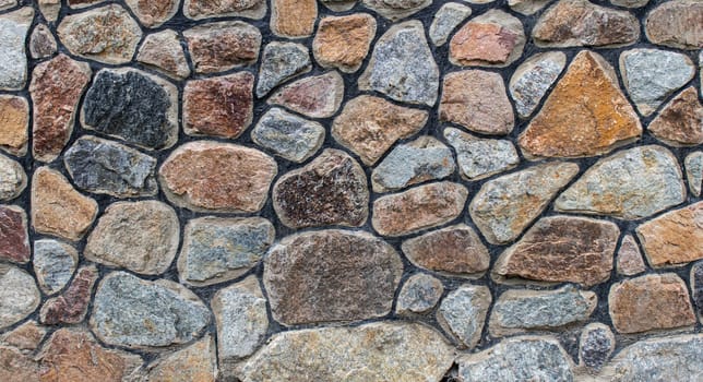 A decorative wall made of multicolored stones with rugged mortar joints, displaying a natural and textured design perfect for rustic or architectural settings.