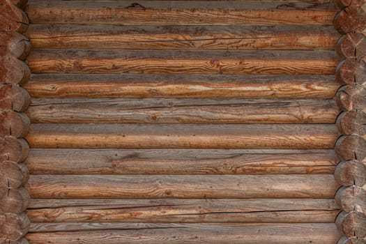 A close-up view of a log cabin wall featuring horizontally aligned wooden logs with visible grain, rough textures, and a warm rustic appearance.