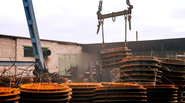 A crane is lifting large, stacked metal containers in an industrial yard. The environment is cluttered with machinery and equipment, suggesting ongoing work and activity.