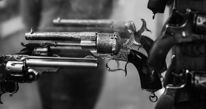 A variety of vintage revolvers are showcased in a gun shop, highlighting intricate details and craftsmanship during the evening.