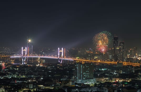 Bangkok, Thailand 31 Dec, 2024 - Night view of Skyscrapers with Colorful fireworks light up sky over Thotsamarachan Bridge (Rama IX Bridge) crossing Chao phraya river. Beautiful city of Bangkok with bright glowing lights of New Year celebration fireworks, use it as your Wallpaper, Poster and Space for text, Selective focus.