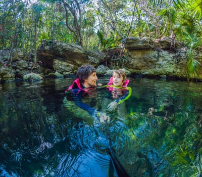 09.12.24, Playa Del Carmen, Mexico: Father and son tourists in the water of a cenote at Xcaret park wearing marked life jackets. Mexican tourism in natural parks. Family bonding, eco-tourism, and adventure concept in Quintana Roo.