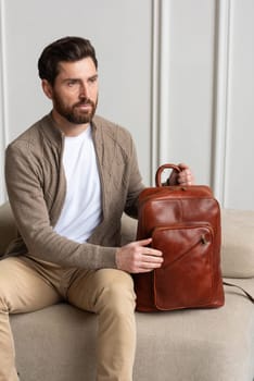 A fashionable man sits with a yellow brown backpack in a contemporary room, embodying urban style and professionalism.