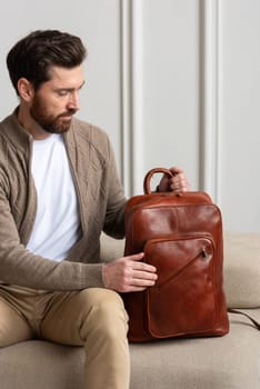 A fashionable man sits with a yellow brown backpack in a contemporary room, embodying urban style and professionalism.