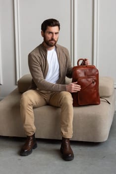 A fashionable man sits with a yellow brown backpack in a contemporary room, embodying urban style and professionalism.