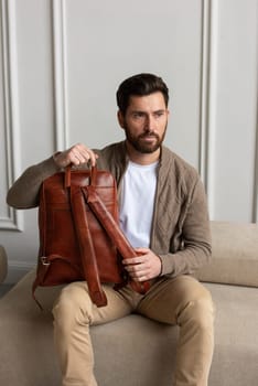 A fashionable man sits with a yellow brown backpack in a contemporary room, embodying urban style and professionalism.