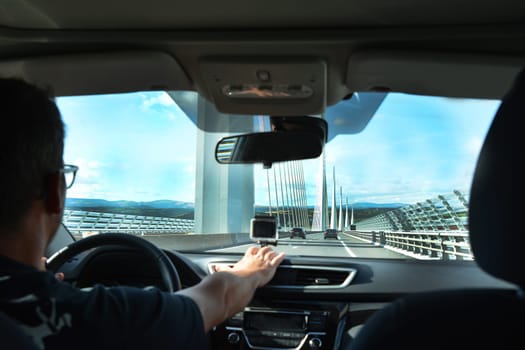 A man in a car traveling on a modern bridge