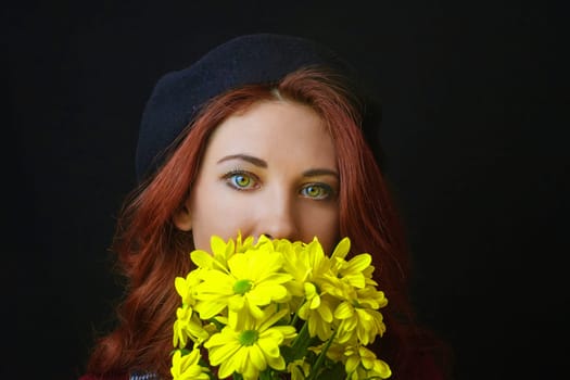French redhead woman in black beret holds and sniffs yellow chrysanthemums