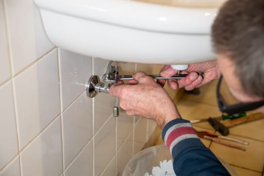 Hands of owner using wrench to repair sink in tiled bathroom, DIY sink installation concept at home,