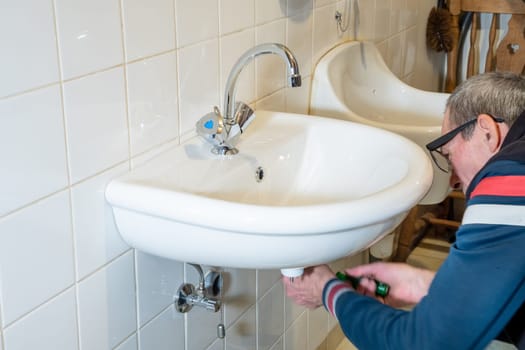 Hands of owner using wrench to repair sink in tiled bathroom, DIY sink installation concept at home,