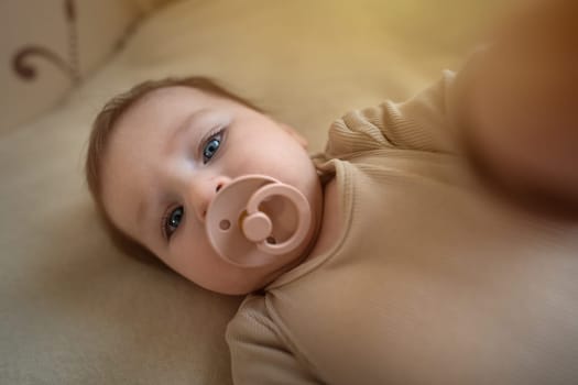 Beautiful baby girl in brown clothes with soother making selfie. Adorable kid portrait. 5 month old child. High quality photo