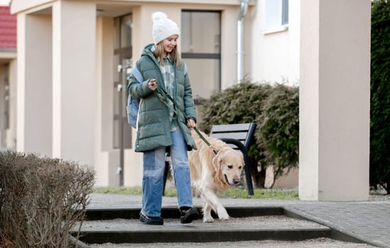 Girl In Green Jacket Walks With Golden Retriever On City Street In Early Spring