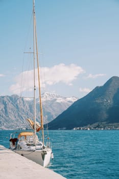 Small white sailing yacht is moored to a pier against the background of mountains. High quality photo