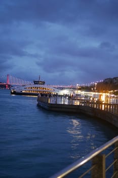 The serene waterfront view at dusk shows city lights reflecting on the calm water