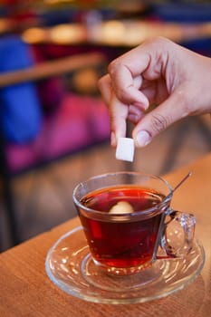 A hand delicately holding a sugar cube high above a steaming cup of rich coffee